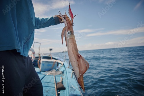 Quadro su tela Fisherman standing on a boat and holding up a large squid