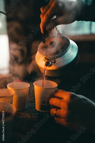 Vertical shot of a person pouring hot coffee into cups with a blurry background