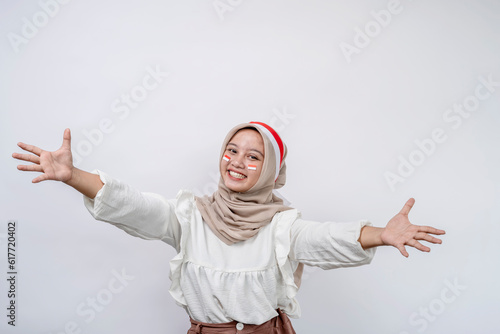 Cheerful young Asian muslim woman celebrating indonesian independence day holding arms wide open for free hugs and smiling happily, welcoming, going to embrace. photo