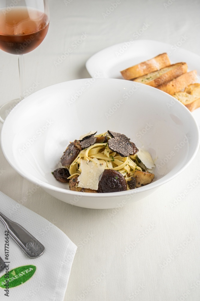 Vertical shot of a gourmet truffle pasta dish near a plate of bread at a restaurant