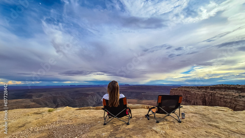 Woman sitting in camping chair enjoying scenic aerial vistas of desert landscape of Valley of the Gods seen from Muley Point near Mexican Hat, San Juan county, Utah, USA. Monument valley in distance photo