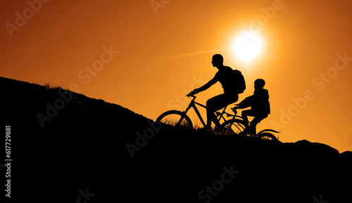 Silhouette of a two person riding a mountain bike uphill. beautiful sunset background. 2 people - daughter, father.