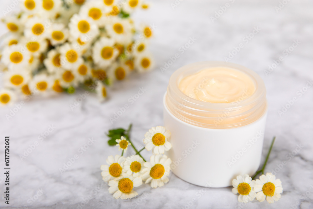 Cream for body and hands with a chamomile flower on a light marble background. Herbal dermatological cosmetic hygiene cream. Natural cosmetic product. Cosmetic tube. Ecological cosmetics.Copy space.