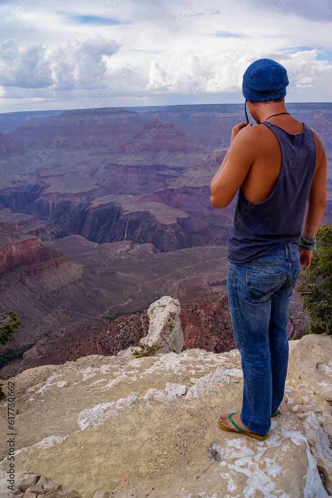 Rear view of man in tank top standing on the edge of a rock on Bright Angel trail with panoramic aerial overlook of South Rim of Grand Canyon National Park, Arizona, USA, America. Amazing vistas Rear view of man in tank top standing on the edge of a rock on Bright Angel trail with panoramic aerial overlook of South Rim of Grand Canyon National Park, Arizona, USA, America. Amazing vistas