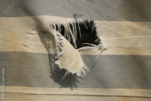 hanging teared rag spread isolated on black background , can use like a background or any texture. hole in the tissue. Unbleached beige fabric with torn stitch, hole and loose threads