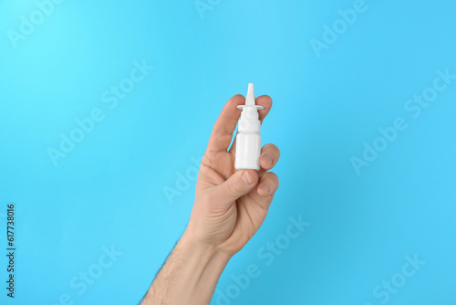 Man holding nasal spray on light blue background, closeup