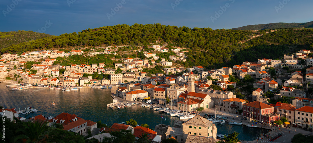 Panorama of Pučišća village on Brac island, Croatia. Mediterranean holiday destination with picturesque harbor fjord in warm summer evening light at golden hour. Idyllic atmosphere in adriatic sea.
