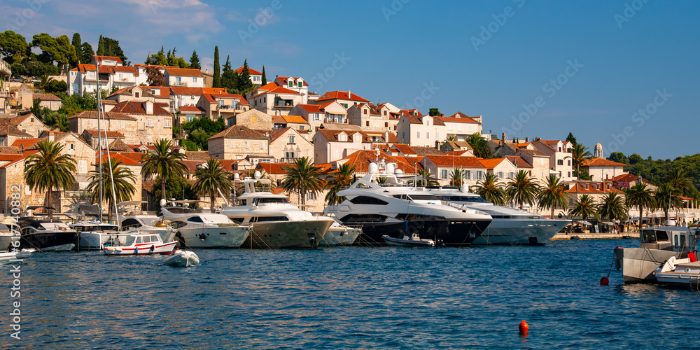 Panoramic view of croatian holiday hot spot old village of Hvar on Hvar island in the Adriatic Sea. Waterfront promenade with motor yachts and fisher boats on a sunny summer day with warm light.