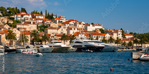 Panoramic view of croatian holiday hot spot old village of Hvar on Hvar island in the Adriatic Sea. Waterfront promenade with motor yachts and fisher boats on a sunny summer day with warm light. photo