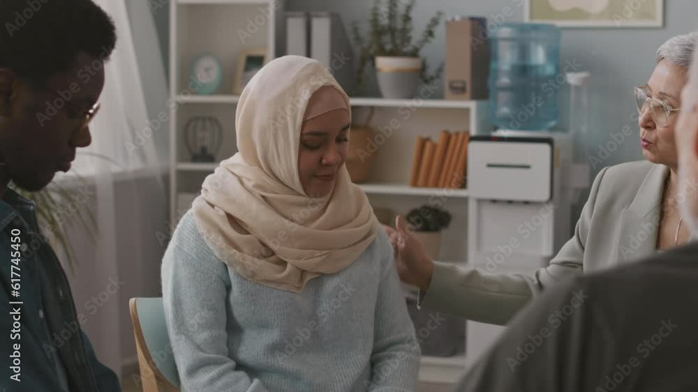 Medium shot of Asian female psychologist and group of multiracial people supporting young Muslim woman sharing her mental problems at therapy session Medium shot of Asian female psychologist and group of multiracial people supporting young Muslim woman sharing her mental problems at therapy session