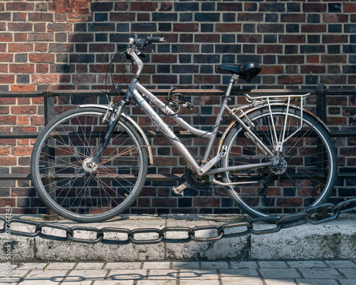 Authentic old bicycle with traces of rust in the sunlight against the background of a medieval brick stone wall behind a vintage metal chain in the foreground, the shadow of the chain in foreground