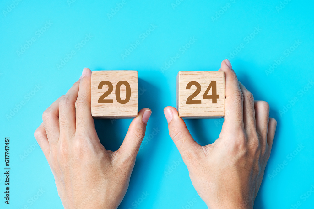 hand holding wooden cube block with 2024 text on blue background. Resolution, plan, review, goal, start and New Year holiday concepts hand holding wooden cube block with 2024 text on blue background. Resolution, plan, review, goal, start and New Year holiday concepts