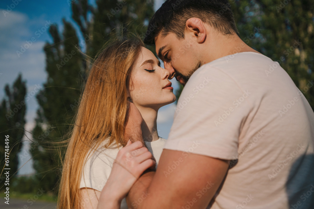 Side view of young man and woman in casual clothes hugging and kissing each other while standing in green forest Side view of young man and woman in casual clothes hugging and kissing each other while standing in green forest
