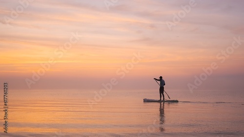 Man paddling on stand up paddle board against background of rising sun. SUP