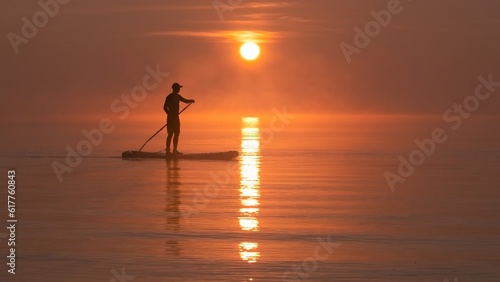 Man paddling on stand up paddle board against background of rising sun. SUP © vadimborkin