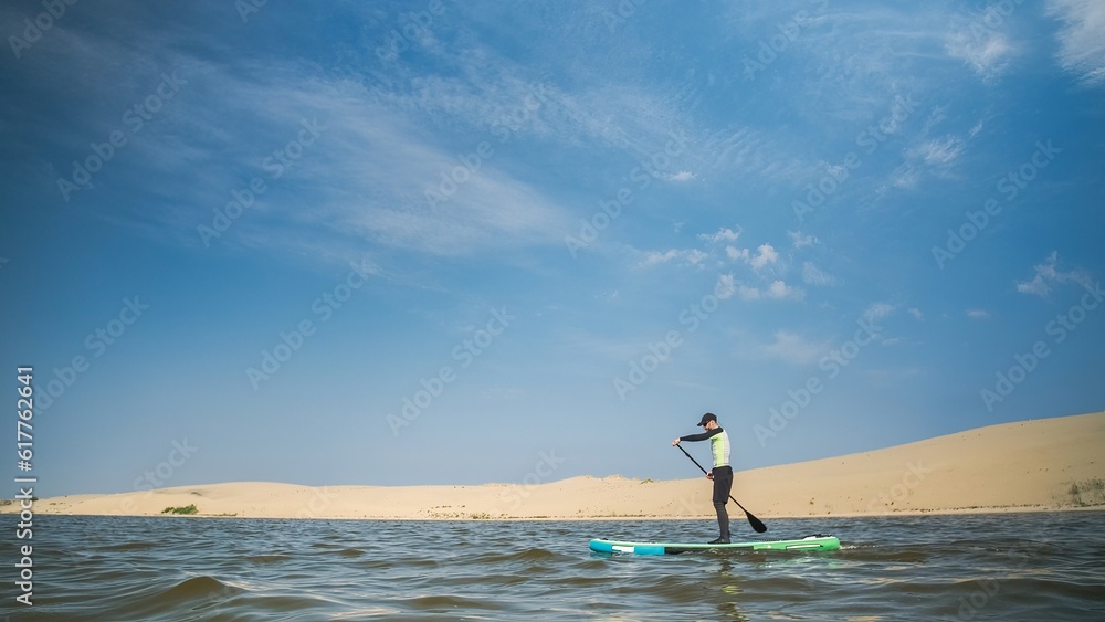 Man paddling on stand up paddle board against background of dunes in desert. SUP