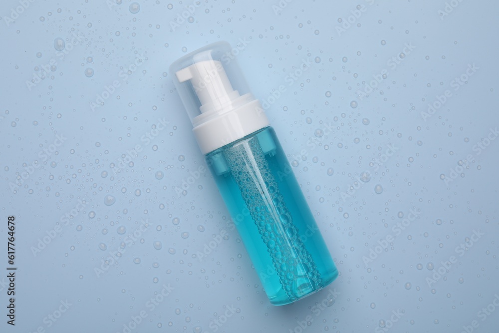 Wet bottle of face cleansing product on light blue background, top view Wet bottle of face cleansing product on light blue background, top view