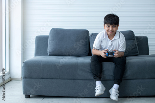 Concentrated Indian boy excited playing video game, sitting on couch and holding controller having fun in gamer emotion, kid gaming addiction concept