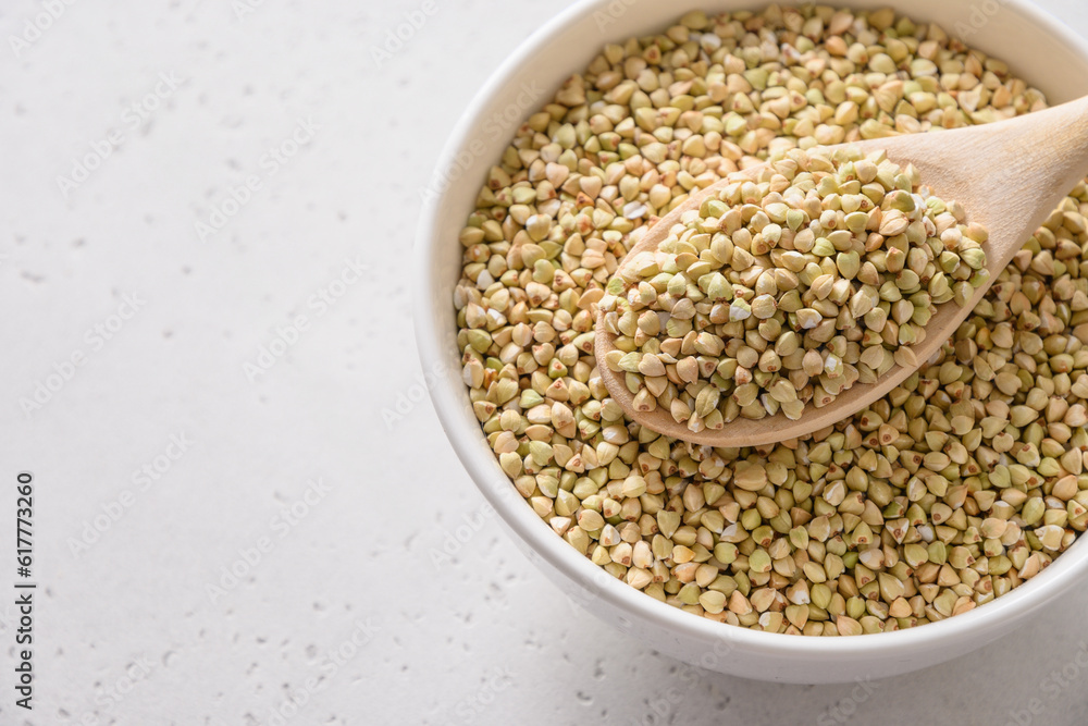 Organic raw green buckwheat in wooden spoon in white bowl on white background. Close up. Copy space. Organic raw green buckwheat in wooden spoon in white bowl on white background. Close up. Copy space.