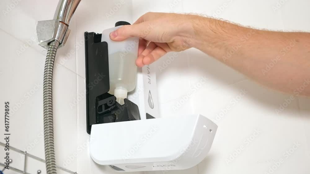 The man opens the Chamber dispenser of soap Duo Shower Gel Shampoo Conditioner and takes out reusable bottles of Wall-mounted white. The man opens the Chamber dispenser of soap Duo Shower Gel Shampoo Conditioner and takes out reusable bottles of Wall-mounted white.