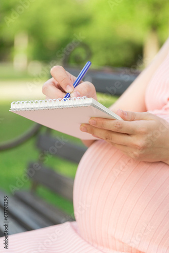 pregnant woman sits on a park bench and writes a to do list to the hospital