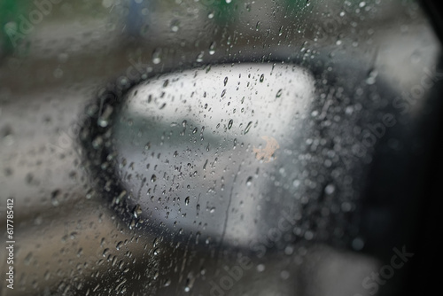 Rainfall on the road. Close up photo with the rear window and mirror of a car covered in rain. Traffic during summer storm.