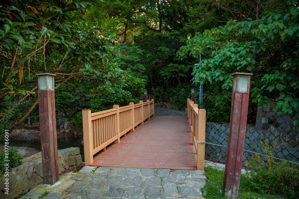 A wooden bridge leading to the mountain in the afternoon in the forest, with a stone path in front of the entrance and two street lamps on both sides.