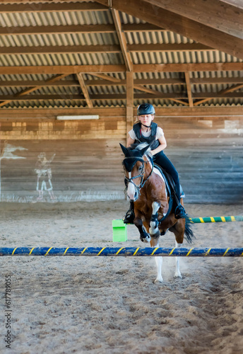 Pretty young girl doing equestrian show jumping on her pony in a farm