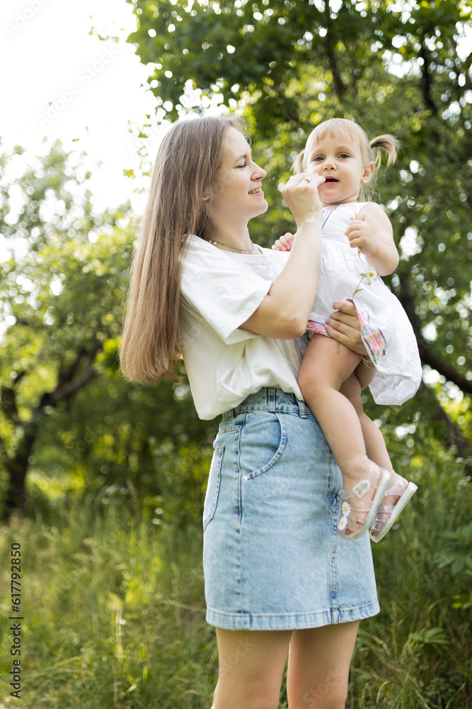 A mother spends time with her two-year-old daughter. Mother and daughter are walking in the garden, hugging and having fun. Mother and her daughter. Maternal love and attachment. Tenderness. A mother spends time with her two-year-old daughter. Mother and daughter are walking in the garden, hugging and having fun. Mother and her daughter. Maternal love and attachment. Tenderness.