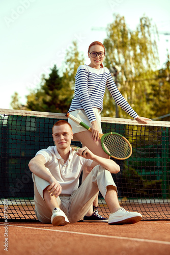 Full-length image of beautiful young woman and handsome man in casual, stylish clothes posing on tennis court on daytime. Concept of casual fashion, sport, active lifestyle, hobby, leisure time, ad © master1305