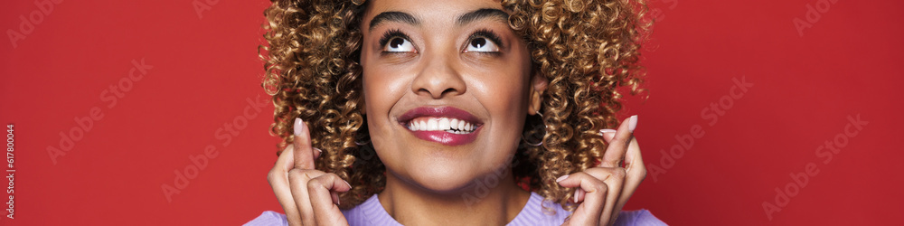 Young black woman with afro curls smiling and holding fingers crossed Young black woman with afro curls smiling and holding fingers crossed