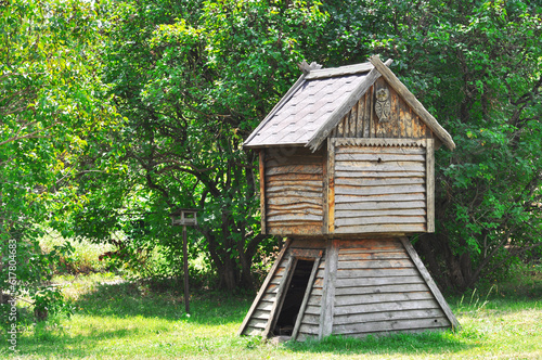Children's fairy-tale wooden hut with a wooden owl on a sunny meadow against the background of green trees