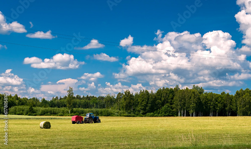 Agricultural countryside landscape with tractor and haystacks, forest on hori...