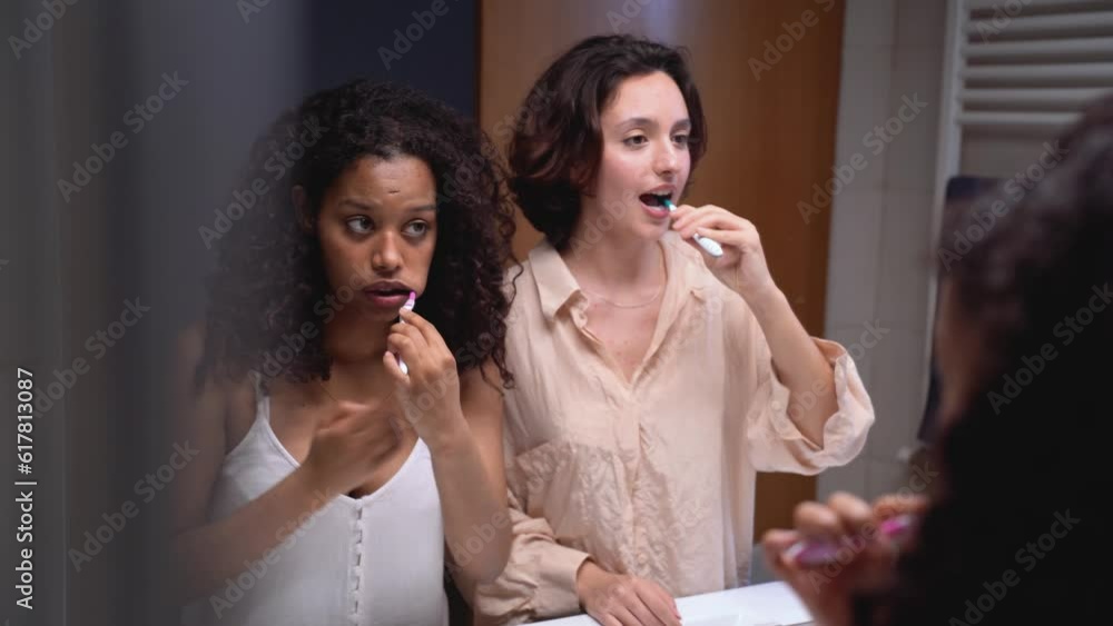 Young diverse women standing and brushing teeth together Young diverse women standing and brushing teeth together