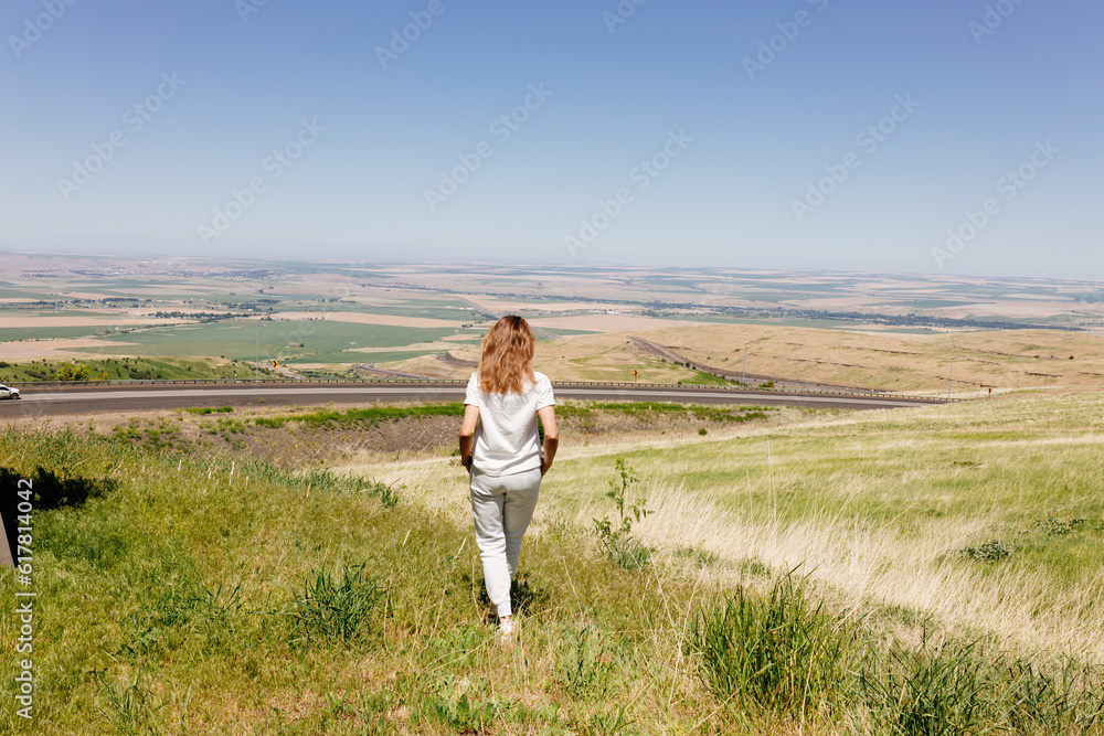 Beautiful summer landscape with meadows and a road from a bird's eye view. Nature in Oregon. A girl in sportswear with red hair walks in a summer meadow, rests in nature, admires nature