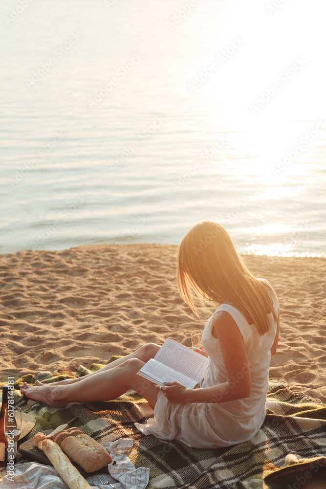 Young woman reading a book at the beach. Back view