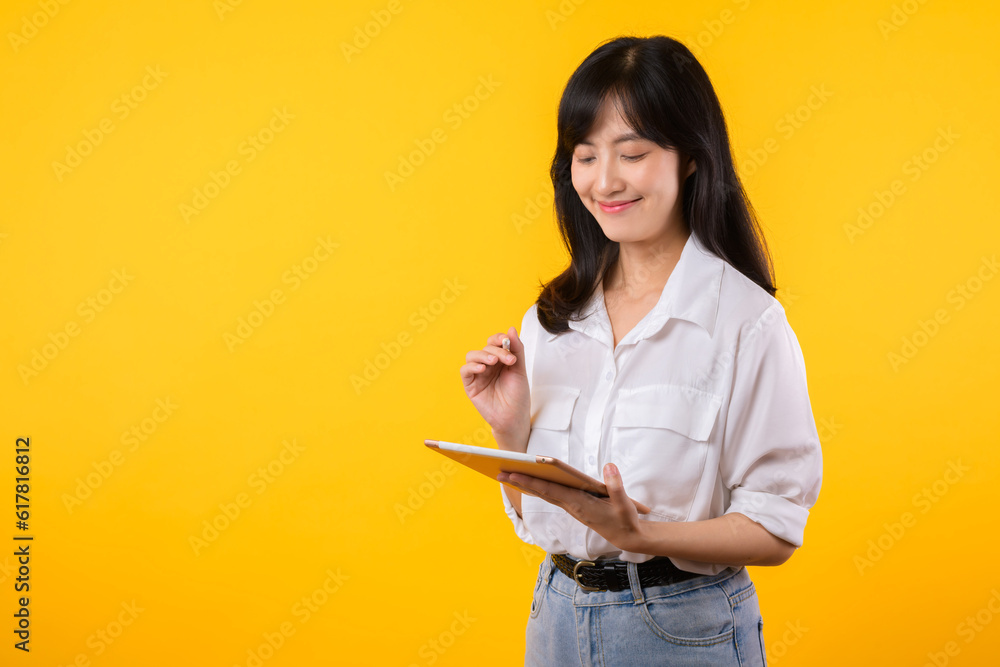 asian young businesswoman happy smile woman wearing white shirt and denim jean plants using tablet business management schedule smiling confident cheerful facial expression against yellow background. asian young businesswoman happy smile woman wearing white shirt and denim jean plants using tablet business management schedule smiling confident cheerful facial expression against yellow background.