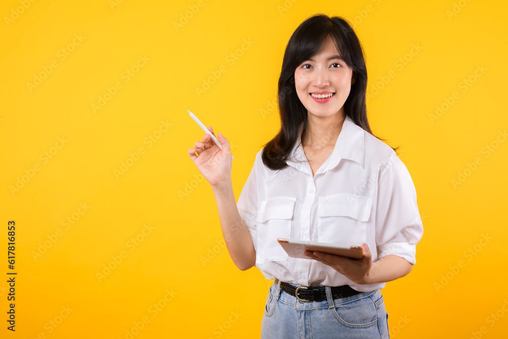asian young businesswoman happy smile woman wearing white shirt and denim jean plants using tablet business management schedule smiling confident cheerful facial expression against yellow background. asian young businesswoman happy smile woman wearing white shirt and denim jean plants using tablet business management schedule smiling confident cheerful facial expression against yellow background.