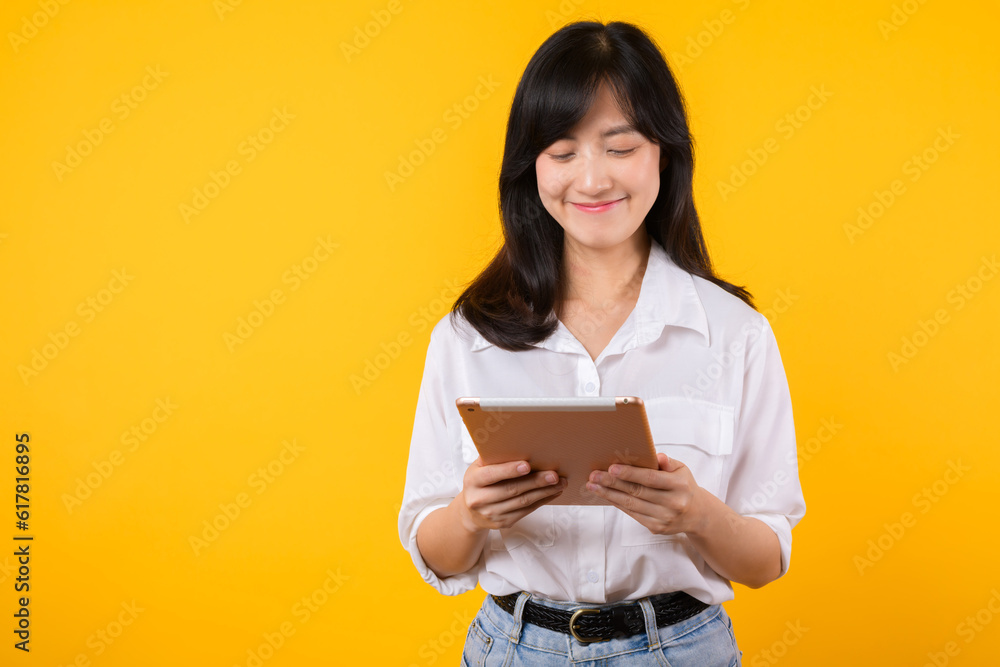 young Asian woman wearing white shirt smiles brightly while holding digital tablet against yellow background, represents a confident company worker embracing modern technology concepts. young Asian woman wearing white shirt smiles brightly while holding digital tablet against yellow background, represents a confident company worker embracing modern technology concepts.