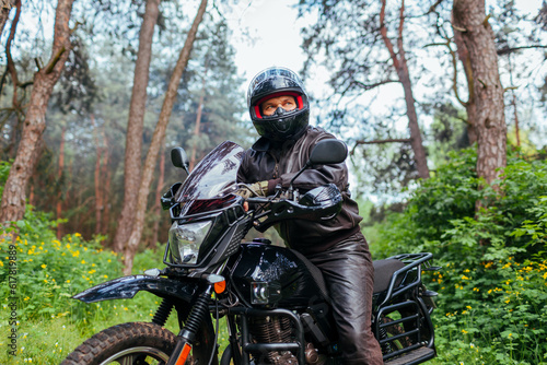 Senior motorcyclist riding motobike outdoors. Man in leather jacket resting after ride in summer forest. Space © maryviolet