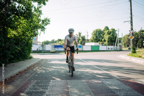 Photo of a sportsman cyclist riding a bicycle on the road outside the city in full gear.