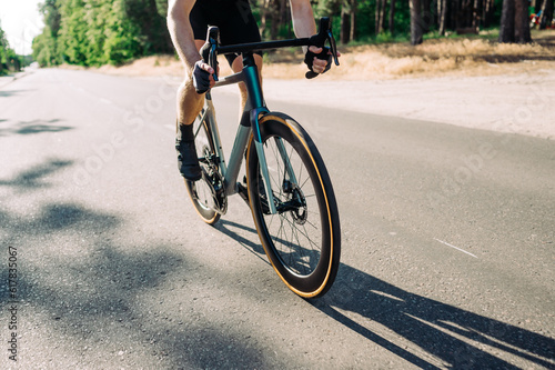 Close-up of a professional road bike and a man in gear riding it in the countryside against a forest background on a sunny day. © bodnarphoto