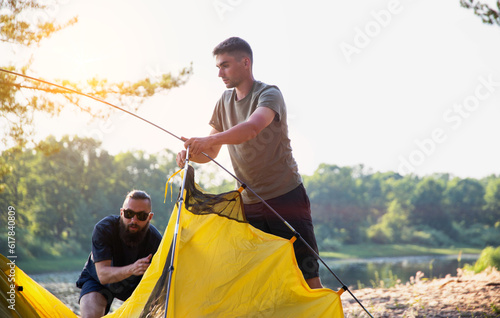 Two guys set up a tent in nature in summer. Tourism as a hobby, copy space for text photo