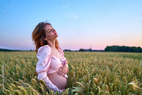 A pregnant woman is holding her stomach in the middle of a wheat field. A girl is expecting a baby at sunset in summer. Fatherhood and motherhood among young people              