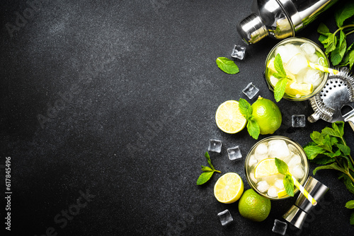 Mojito with rum, lime, mint and ice on black background with bar utensils. Flat lay with copy space.