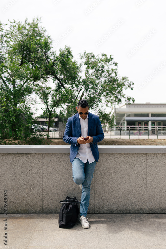 Man using smartphone leaning against the wall