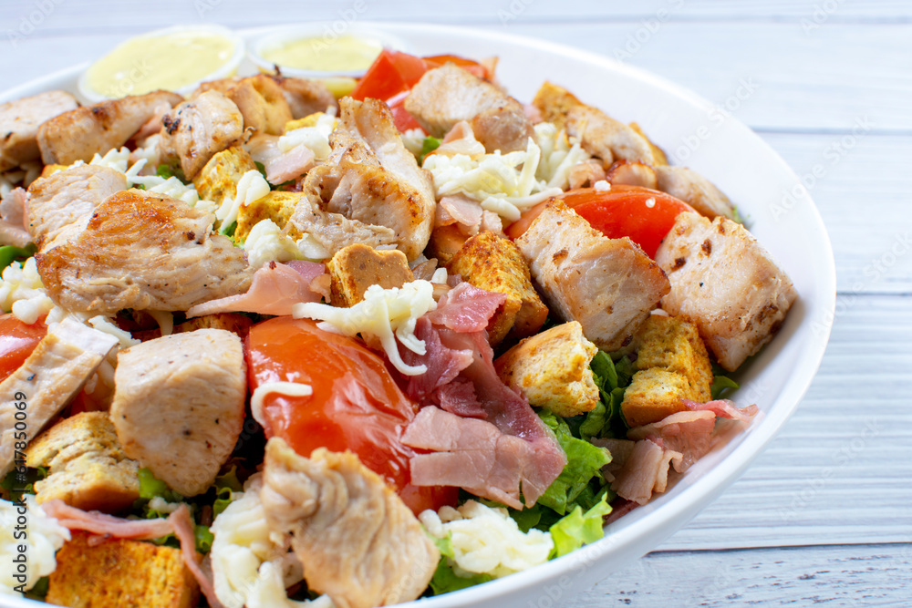 Roasted pork protein salad, accompanied by tomatoes, grated mozzarella cheese, lettuce, bacon, croutons in mayonnaise sauce with mustard