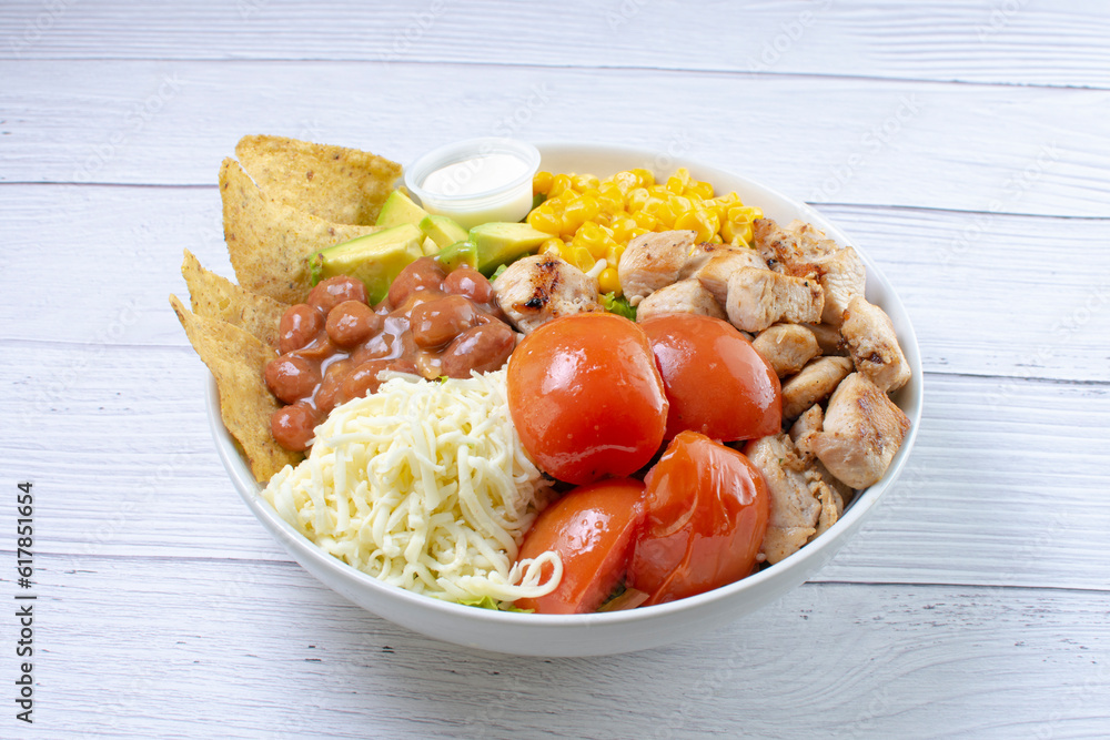 Bowl salad with pieces of roasted pork, grated cheese, beans, corn, tomato, nachos, lettuce, with house mayonnaise