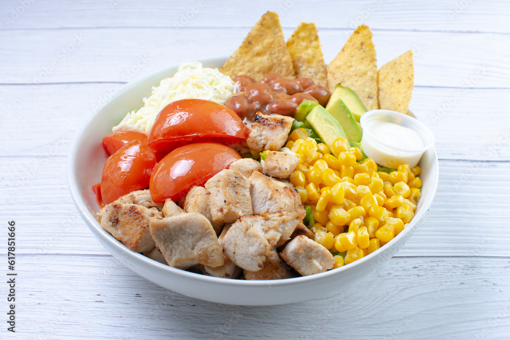 Bowl salad with pieces of roasted pork, grated cheese, beans, corn, tomato, nachos, lettuce, with house mayonnaise