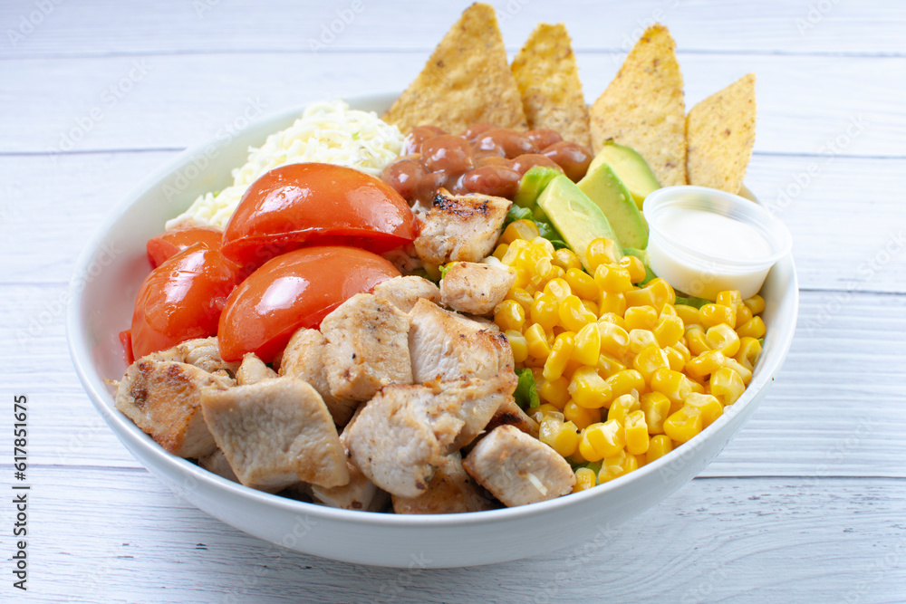 Bowl salad with pieces of roasted pork, grated cheese, beans, corn, tomato, nachos, lettuce, with house mayonnaise